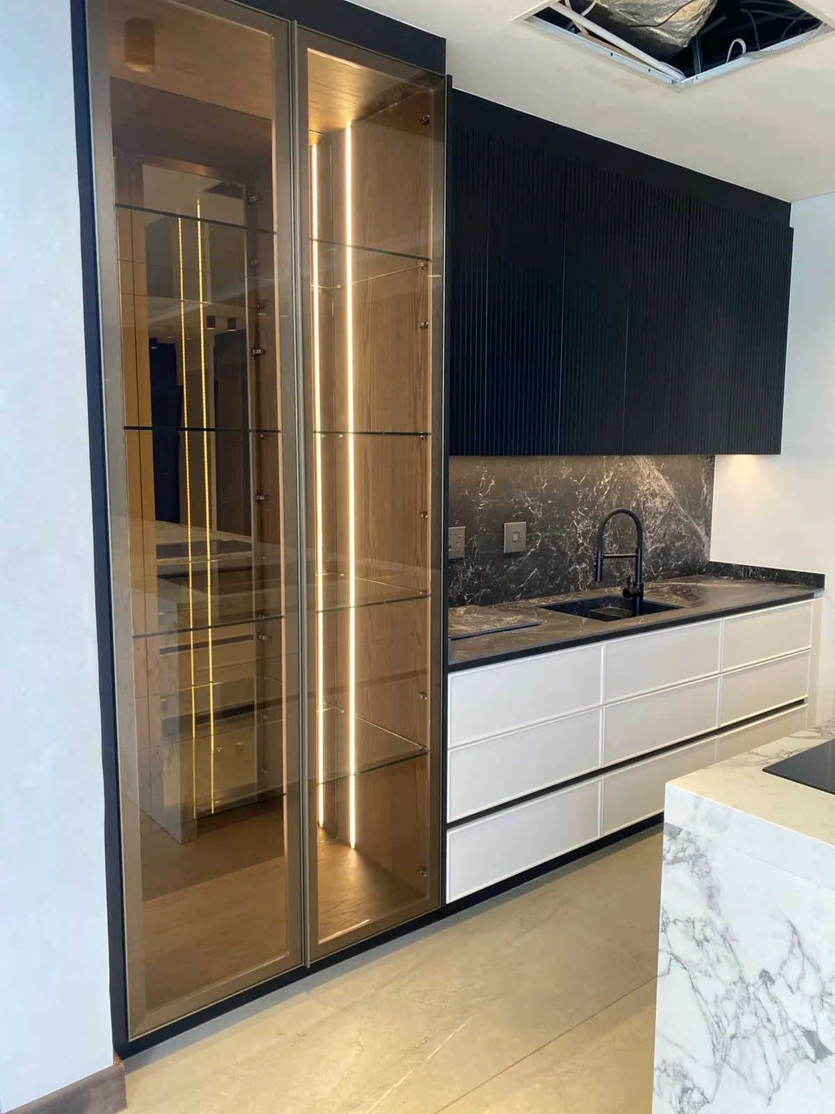 Lit glass display cabinet with white drawer units in a black kitchen